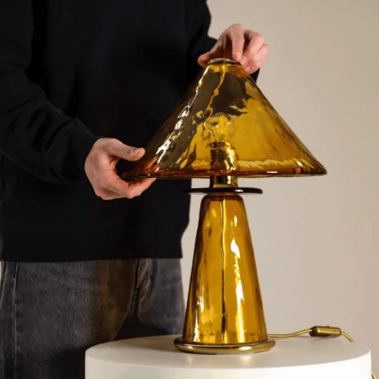Person holding a gold table lamp with a plain background
