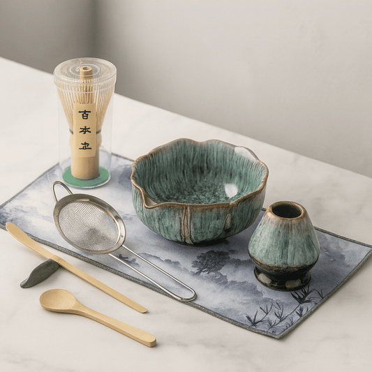 Tea-making set with ceramic bowl, whisk, spoon, and other tools on a decorative mat.
