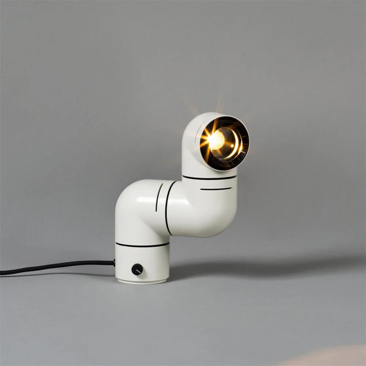 A white elbow-shaped desk lamp illuminating a book with a focused beam of light, placed on a neutral-colored surface.