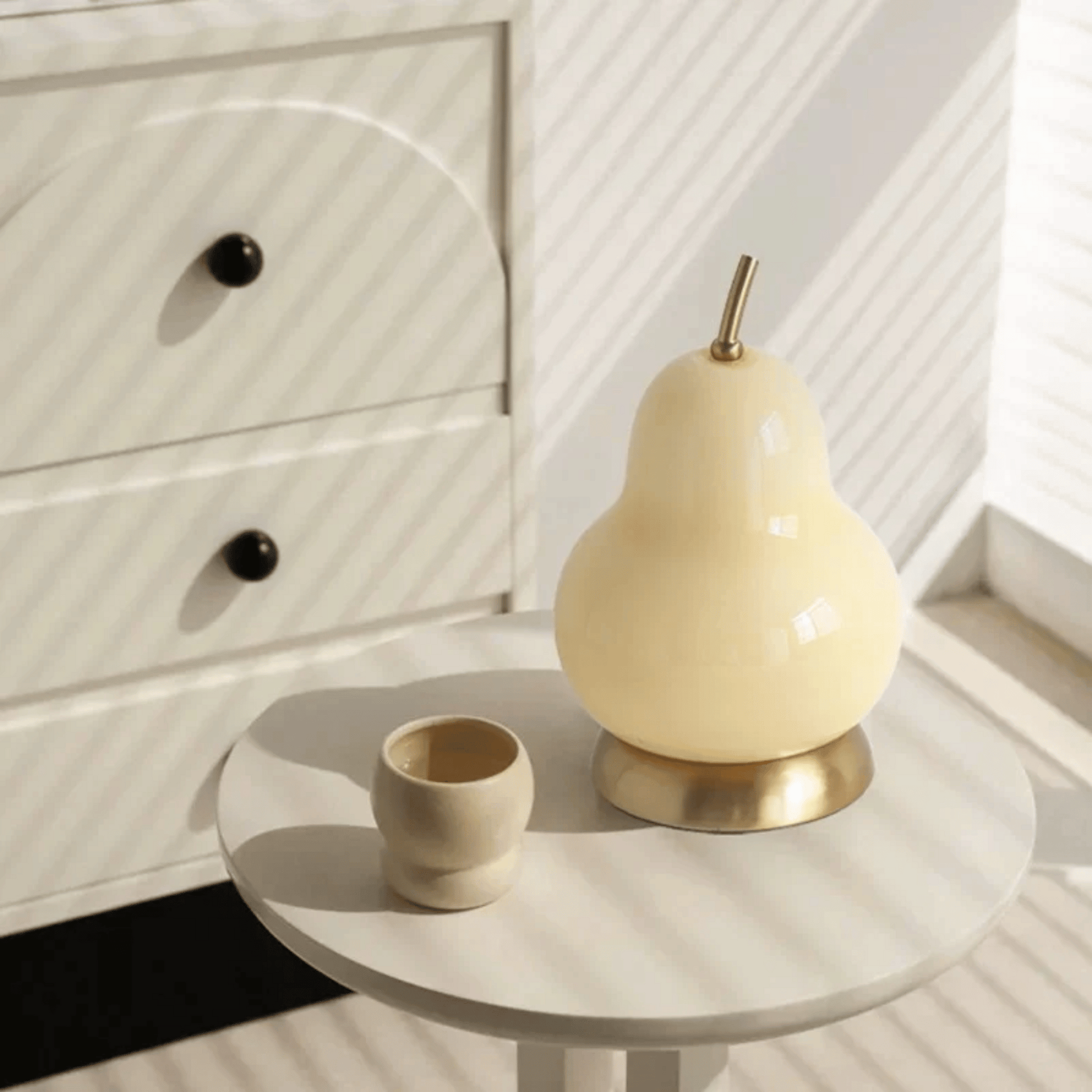 Ceramic pear-shaped lamp on a round table with a white cabinet in the background