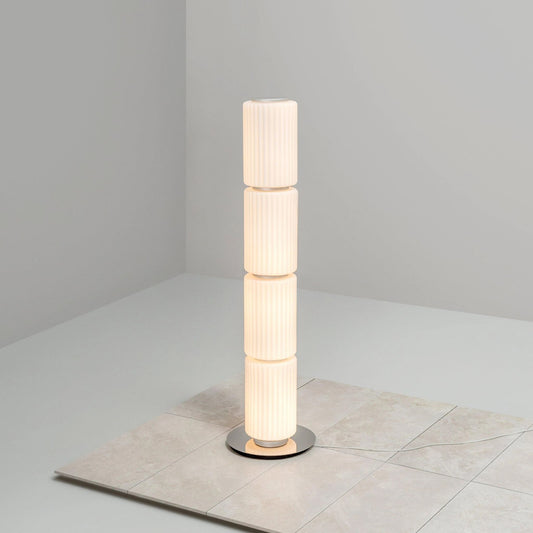 Slim ribbed-glass floor lamp glowing warmly against a light gray wall.