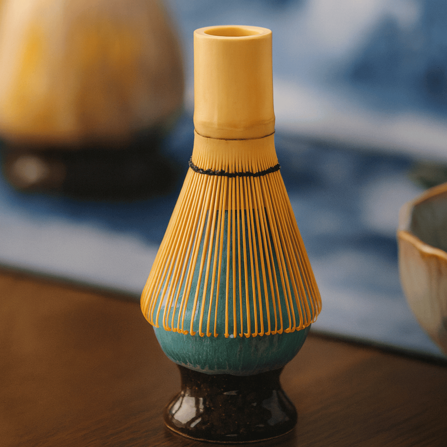Ceramic whisk holder with yellow top and blue base on a wooden surface