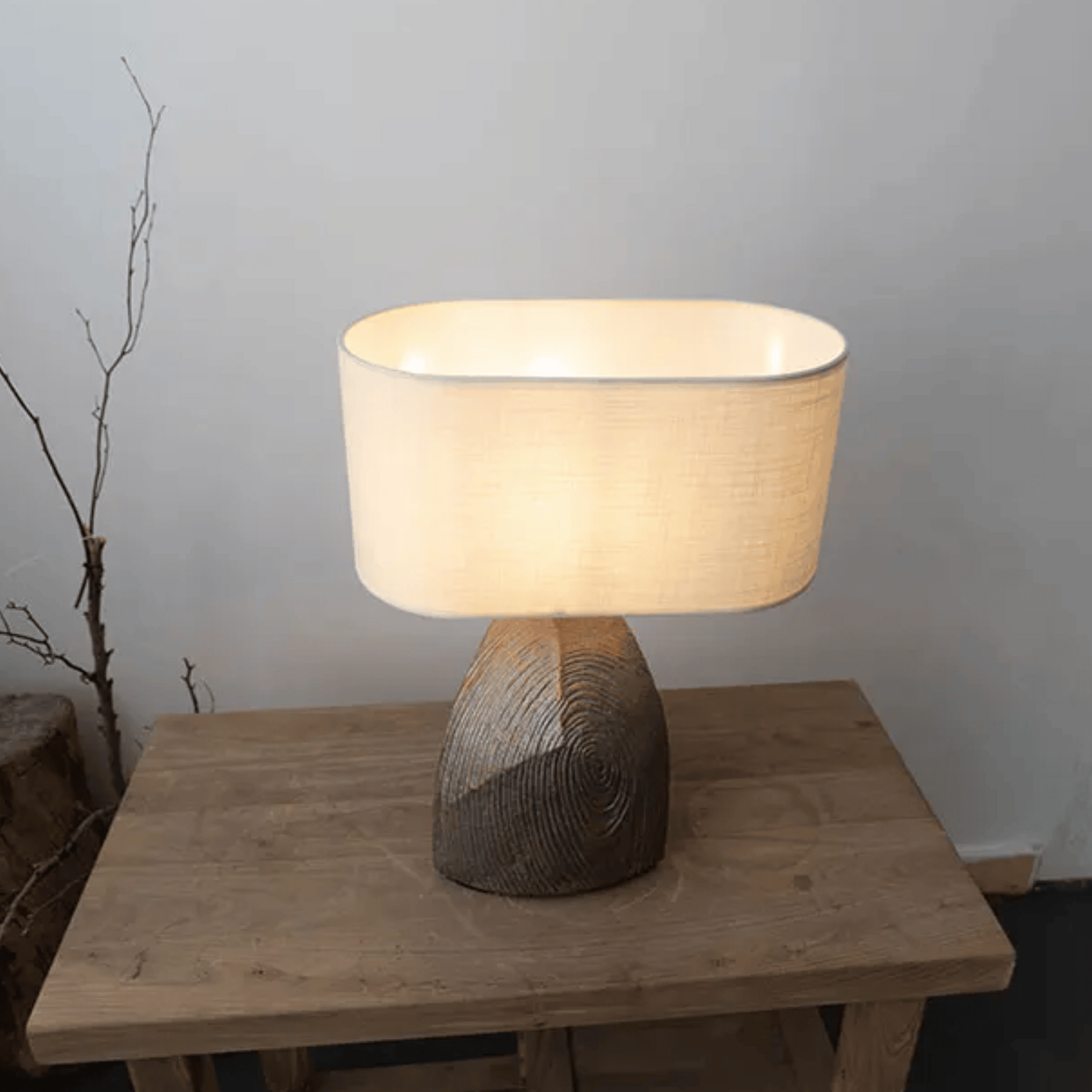 Table lamp with wooden base and beige shade on a wooden table against a plain wall.