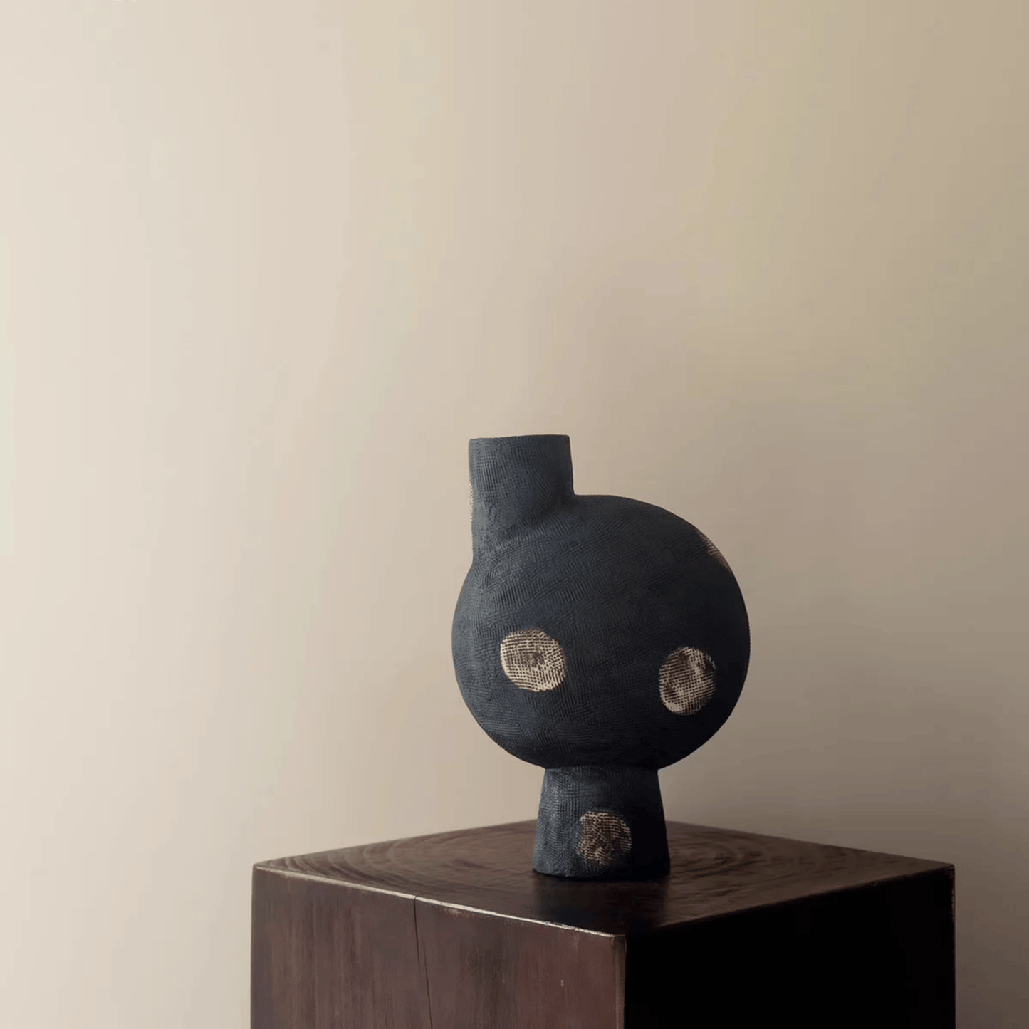Black abstract sculpture on a wooden pedestal against a beige wall