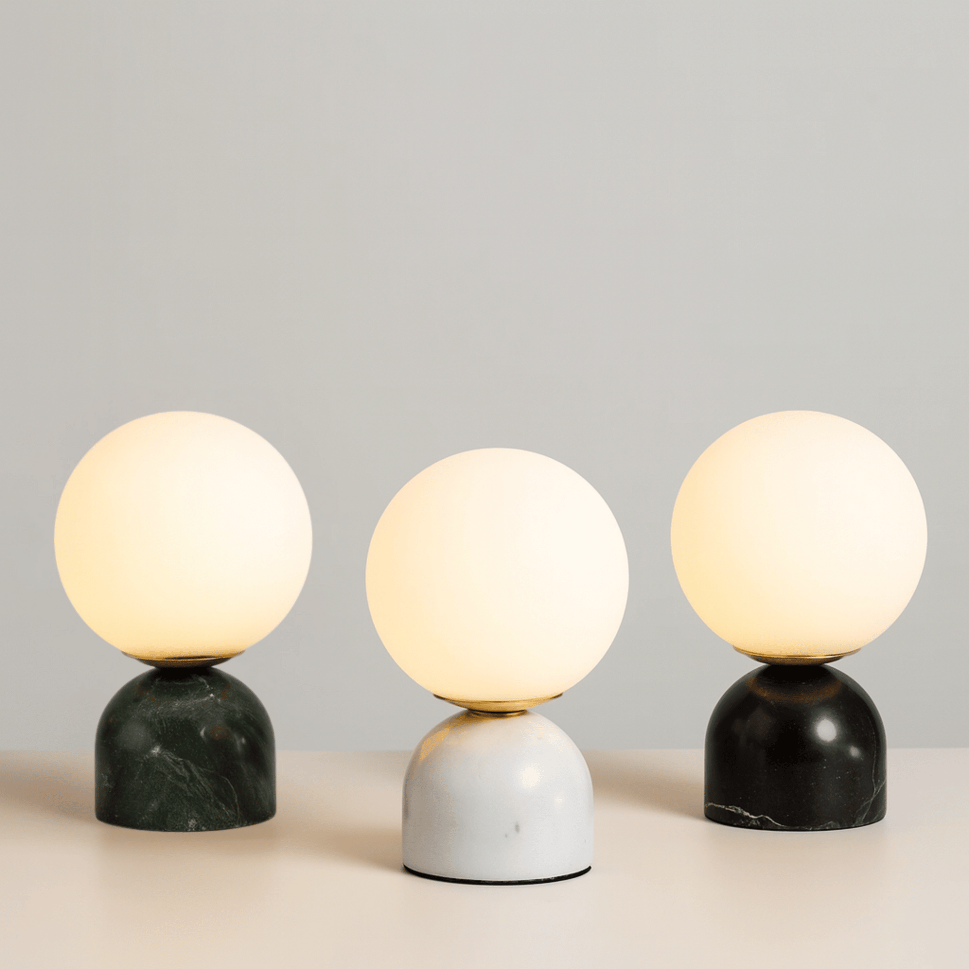 Three spherical table lamps with marble bases on a neutral background