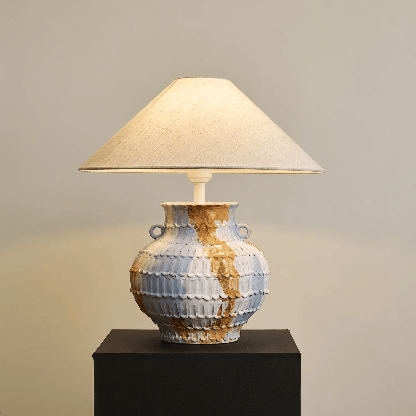 Decorative table lamp with a textured ceramic base on a dark pedestal against a neutral background
