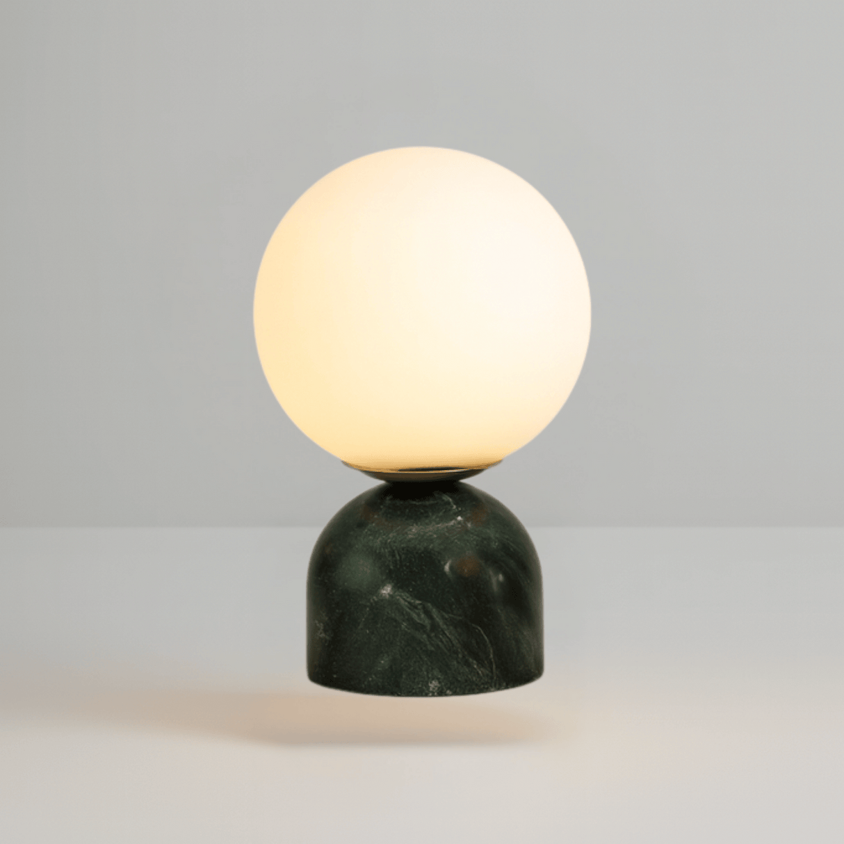 Table lamp with a spherical glass shade and green marble base on a gray background