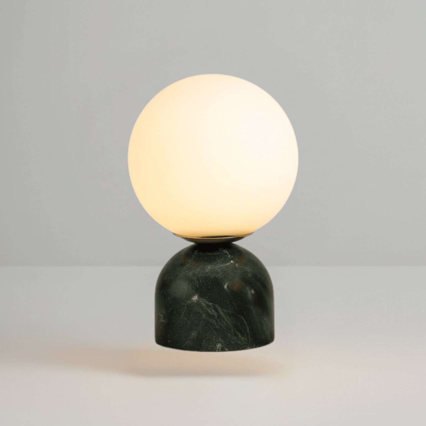 Table lamp with a spherical glass shade and green marble base on a gray background
