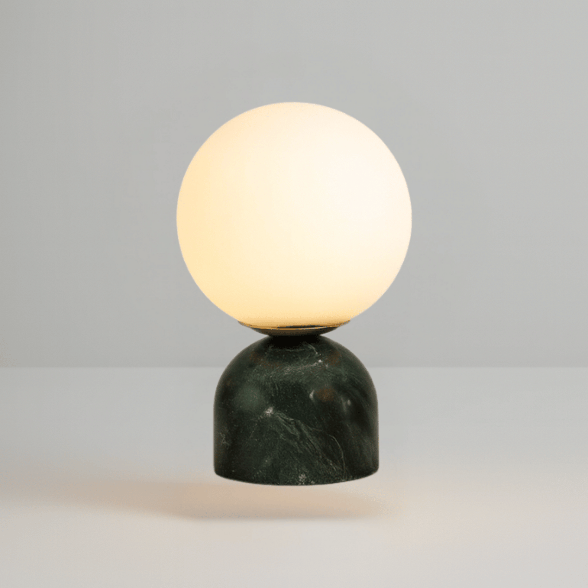 Table lamp with a spherical glass shade and green marble base on a gray background