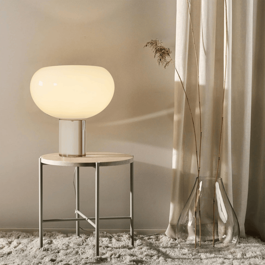 Table lamp on a small round table next to a curtain with decorative vases.