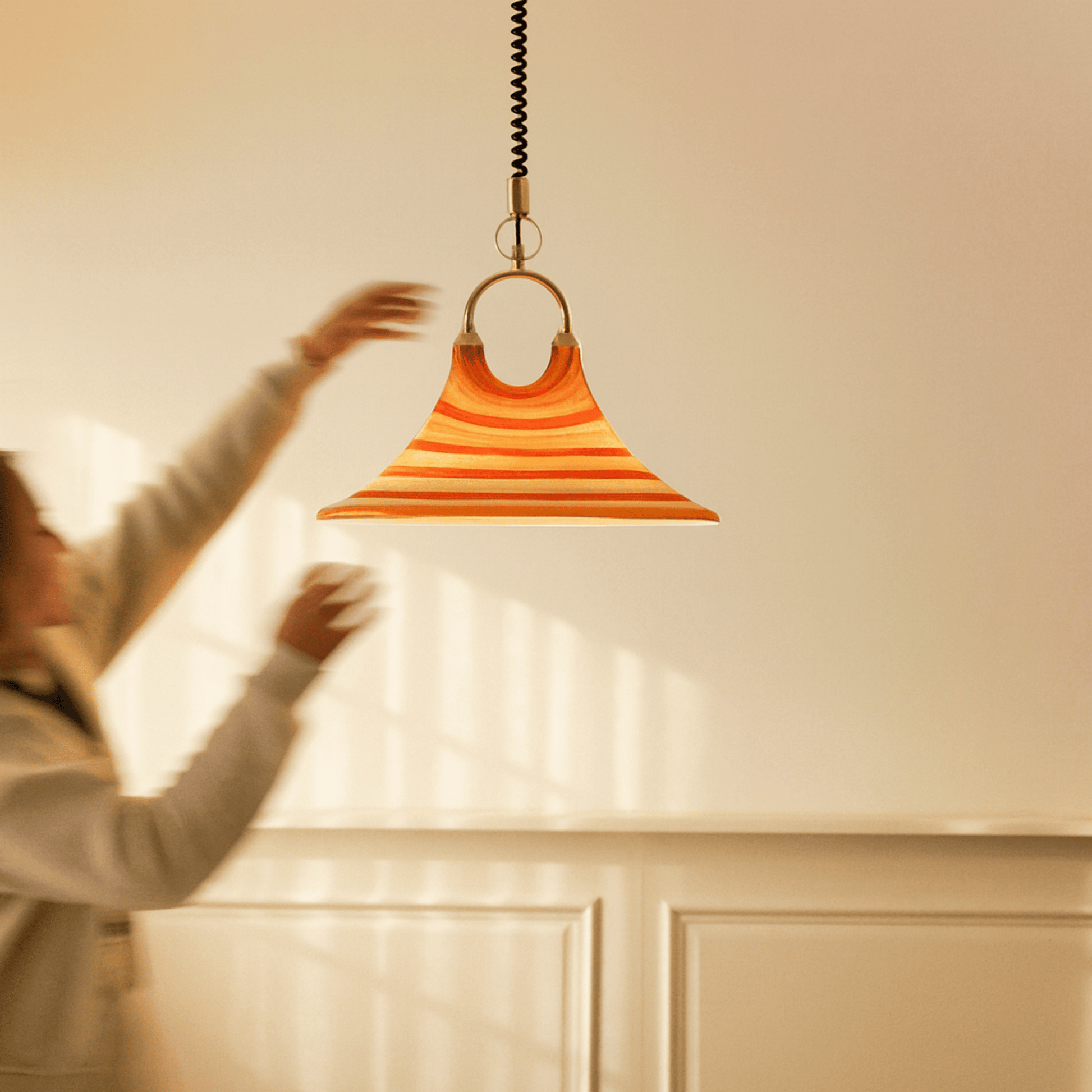 Person adjusting a modern orange pendant light fixture in a room with neutral walls.