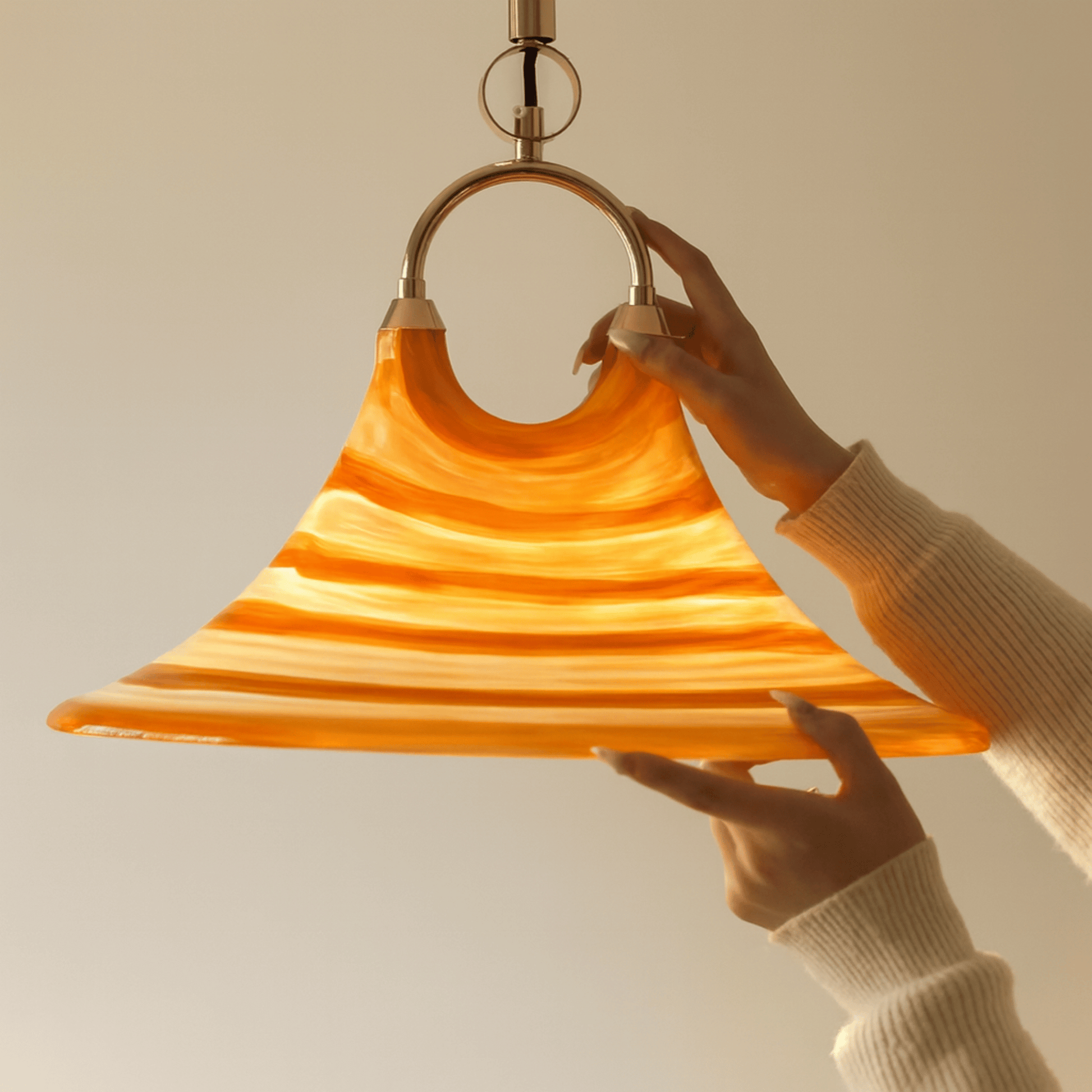 Hand holding a orange and yellow wavy glass pendant light against a neutral background