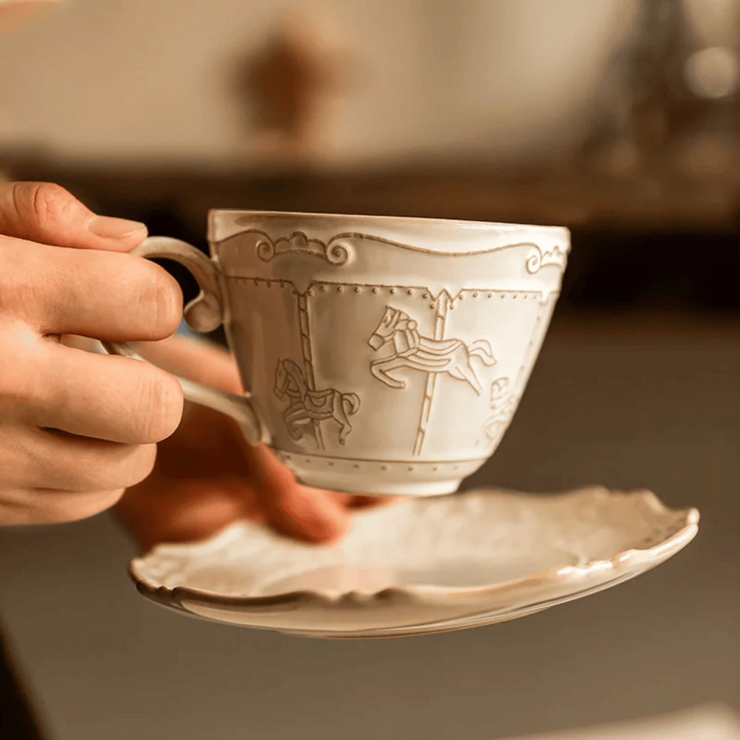 Decorative silver teacup with intricate designs held by a hand against a blurred background