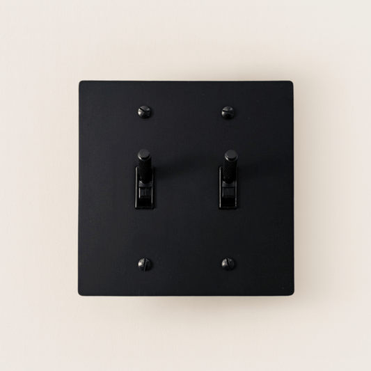 Black square light switch with two toggle switches on a beige background