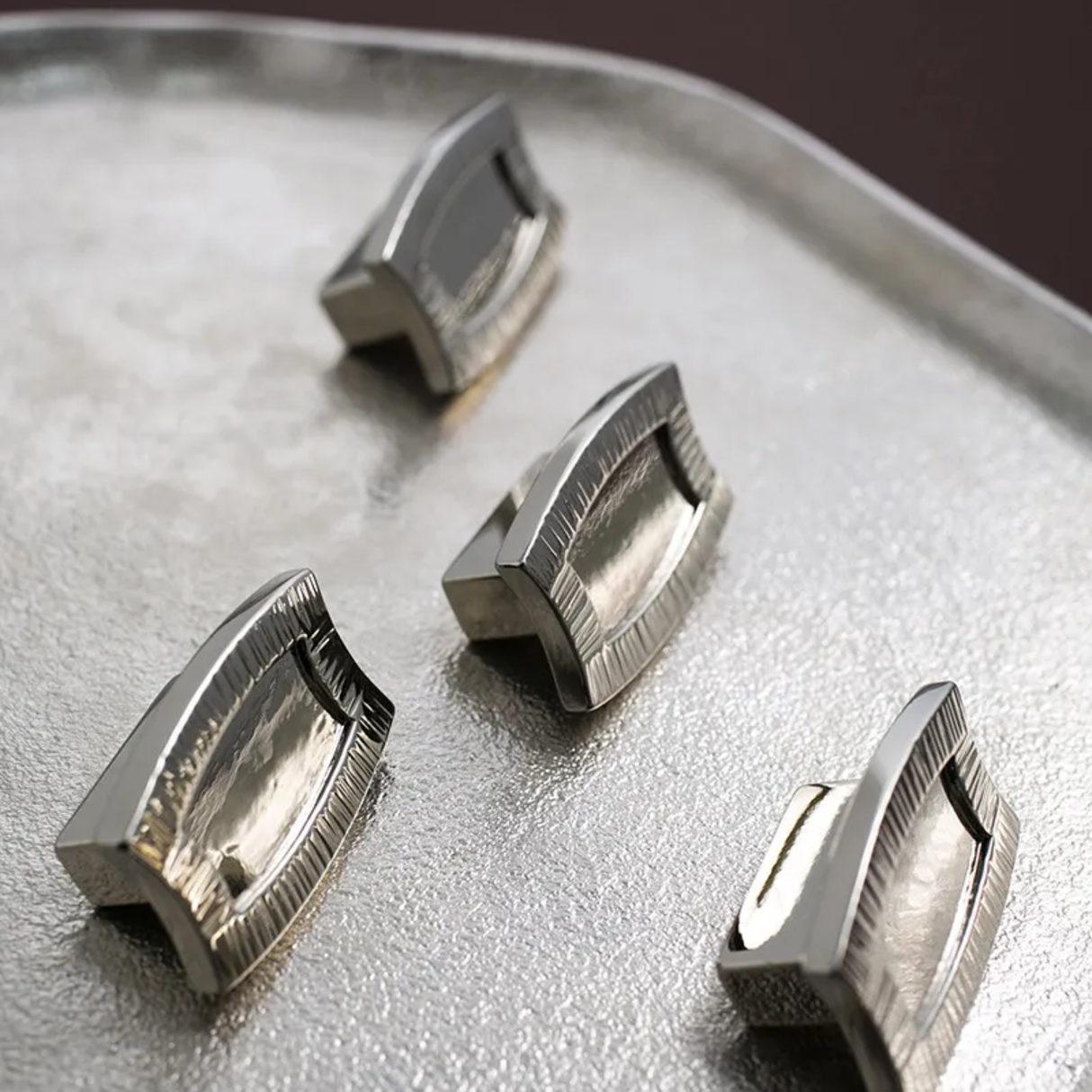 Four metallic cufflinks on a reflective surface