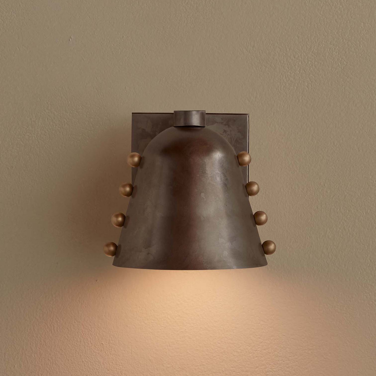 Bronze wall sconce with a warm glow on a beige wall