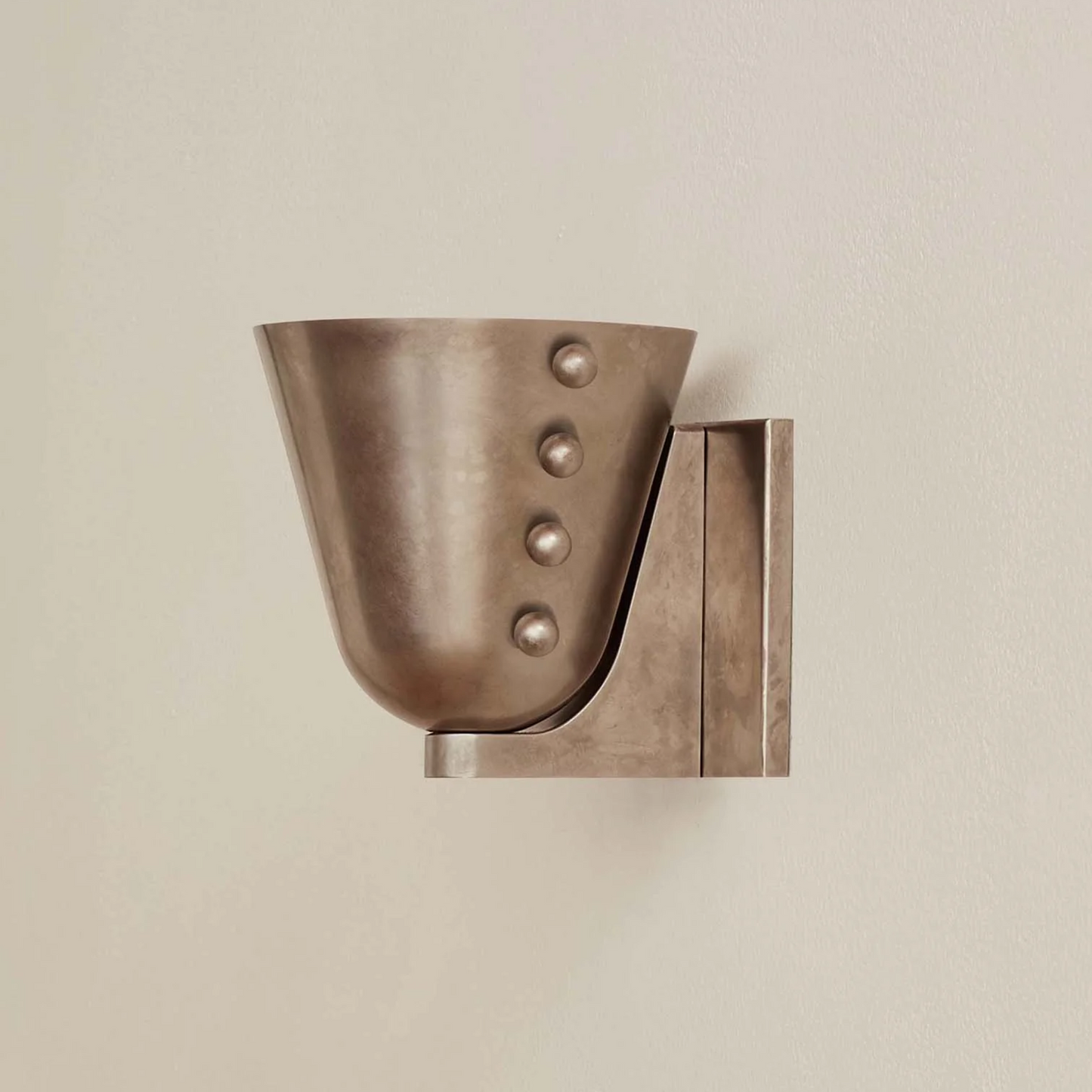Bronze wall-mounted candle holder with decorative elements on a beige background