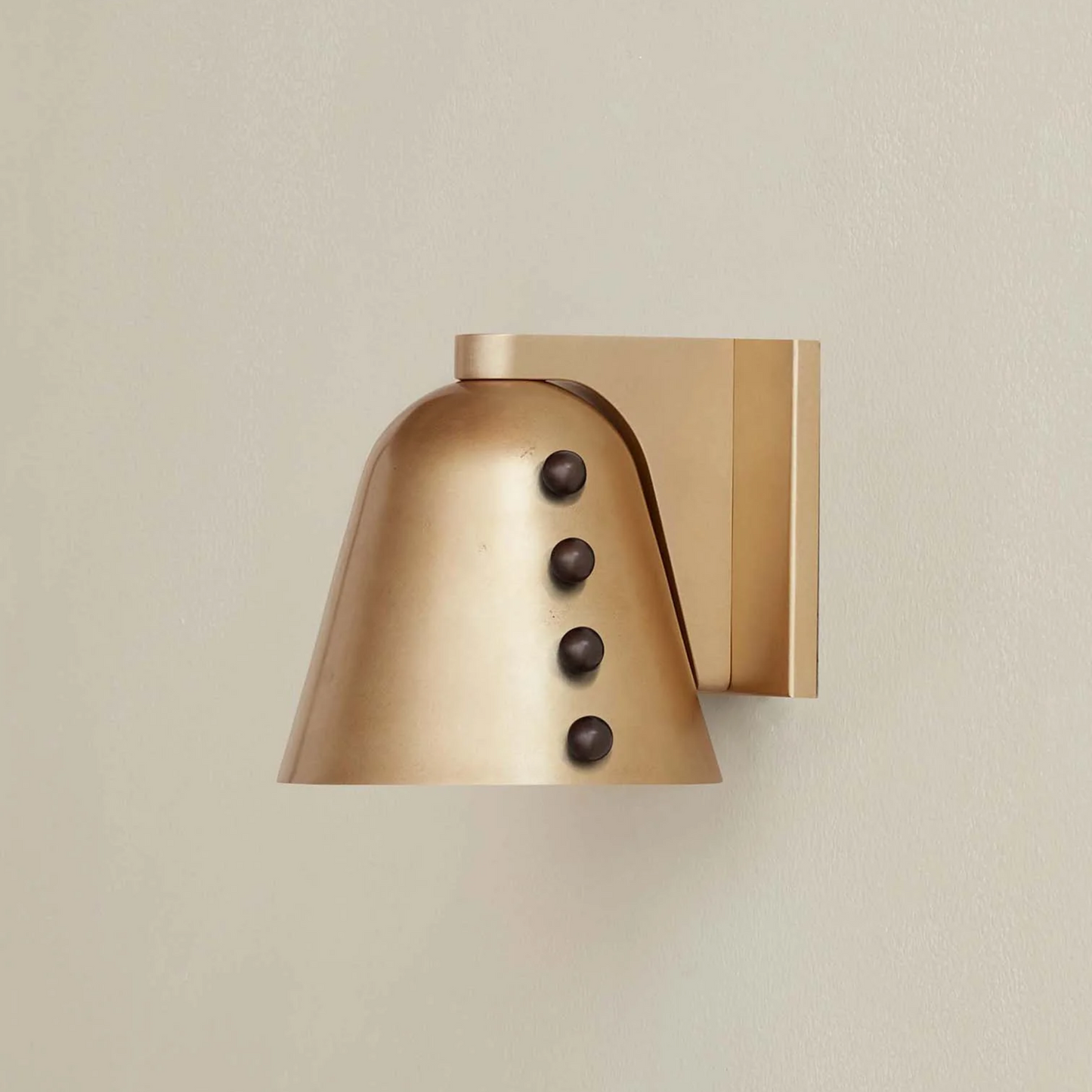 Brass wall sconce with three dark knobs on a beige background
