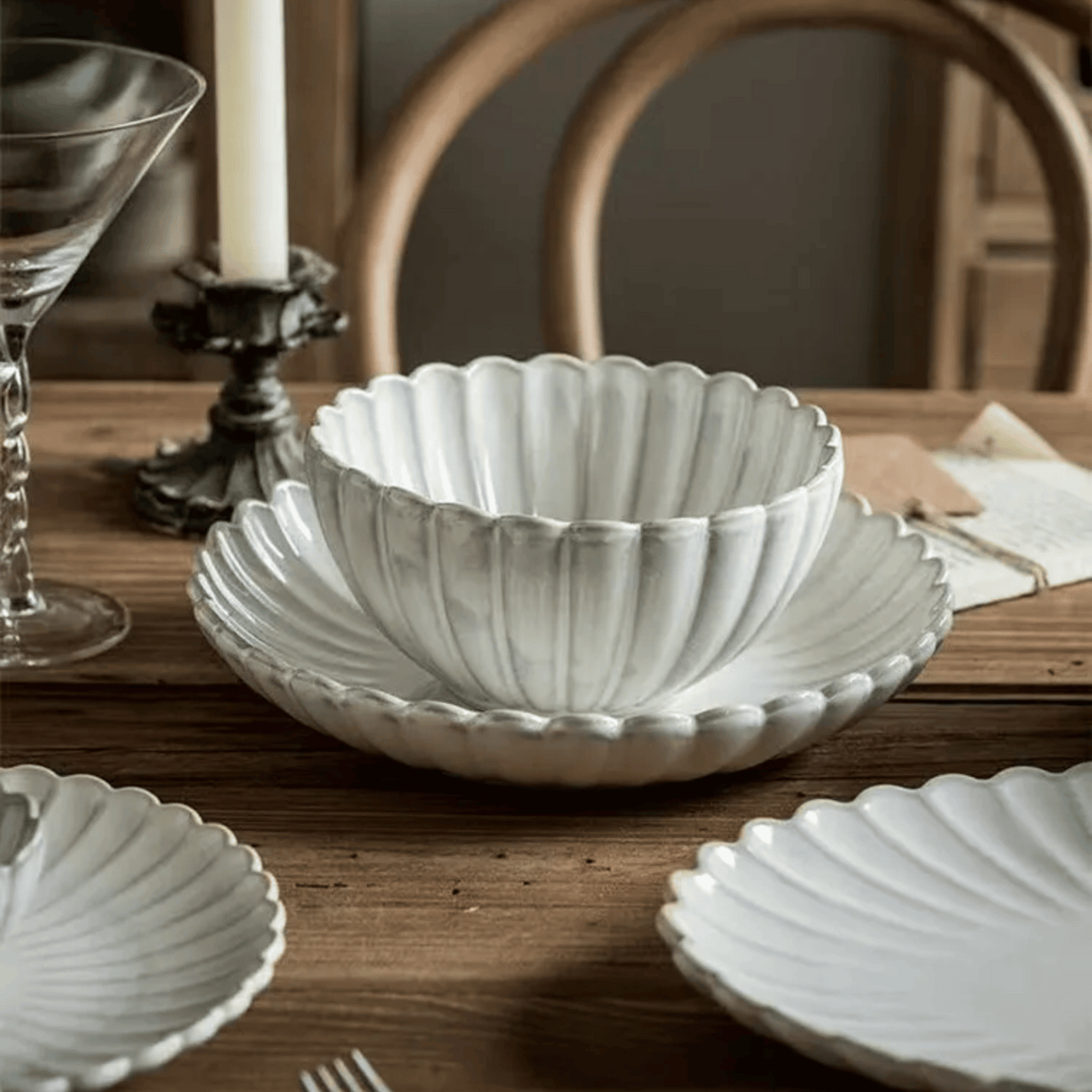 Decorative white ceramic bowl on a wooden table with a candle and glass in the background.