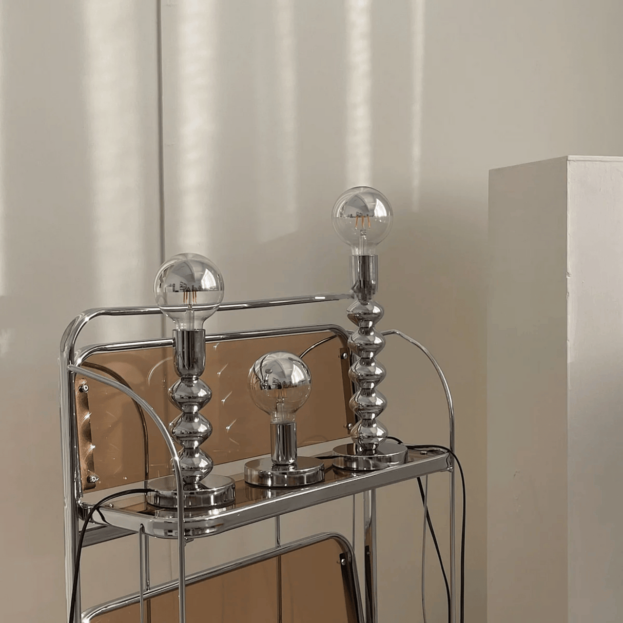Chrome bar cart with three glass light bulbs on a neutral background