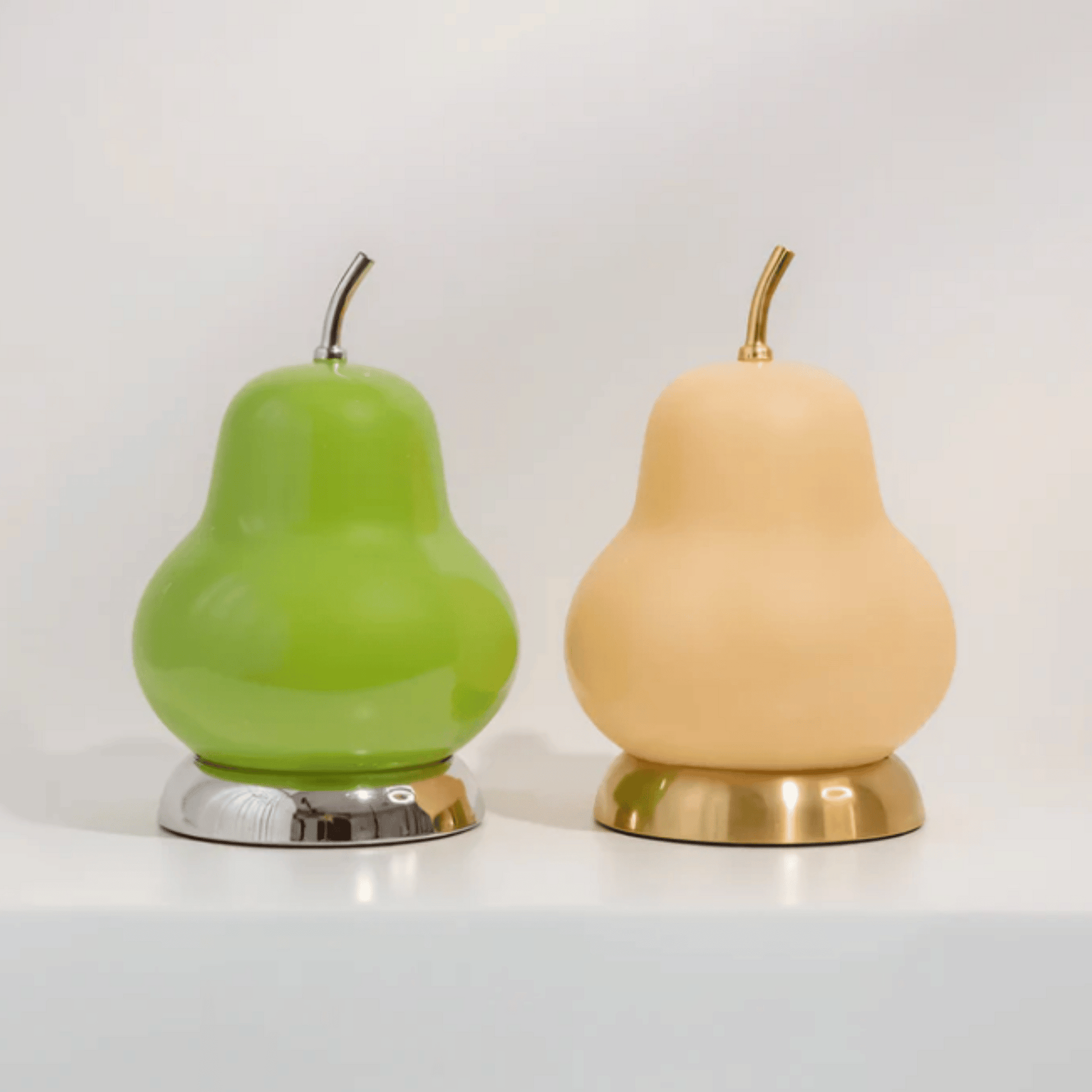 Two pear-shaped lamps, one green with silver base and one beige with gold base, on a white background.