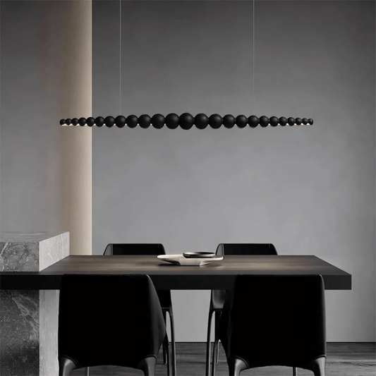 Modern dining area with a long, dark pendant light fixture hanging above a table and chairs.