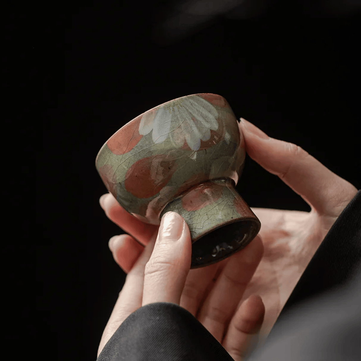 Hand holding a small ceramic cup with floral design against a dark background