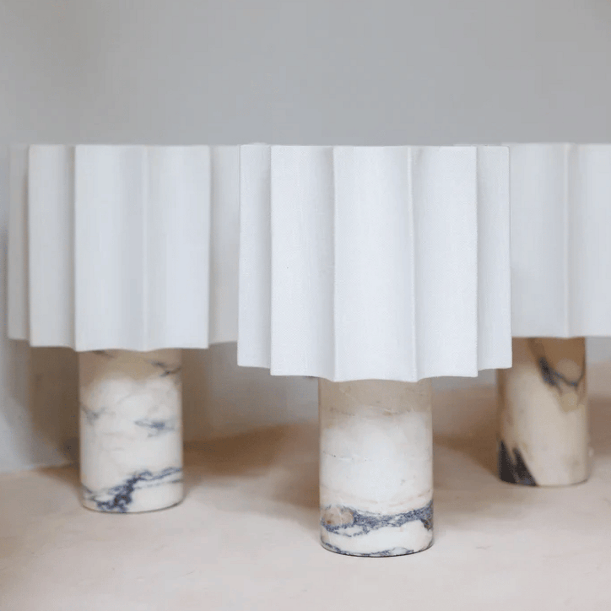 Marble-patterned legs of a table with a white pleated skirt on a neutral background
