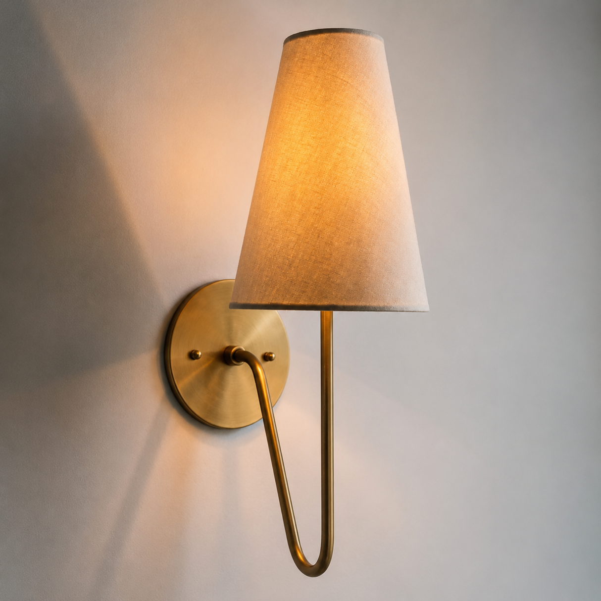 Wall-mounted lamp with a gold fixture and beige shade on a gray wall.