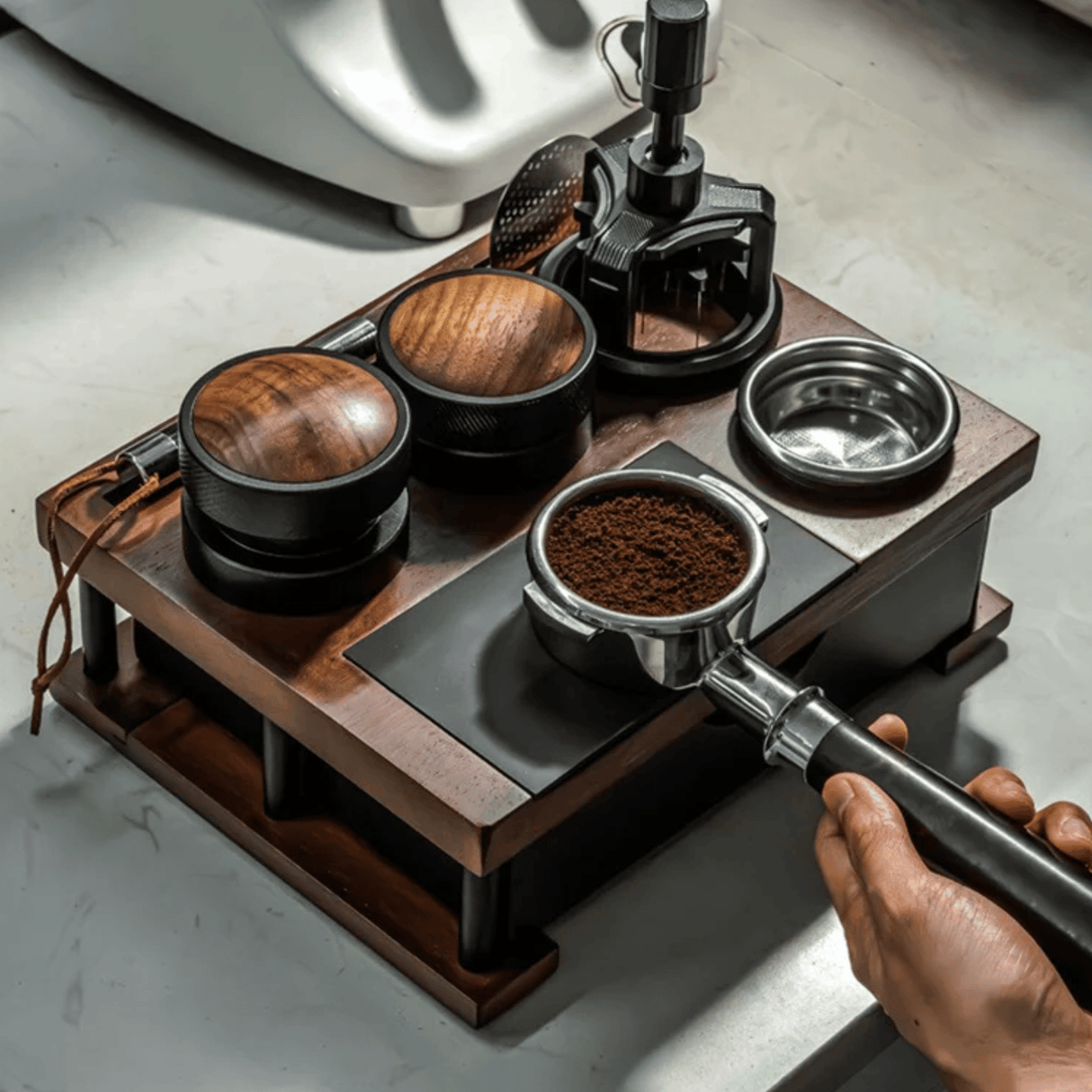 Hand holding a coffee scoop over a wooden coffee grinder with coffee grounds.