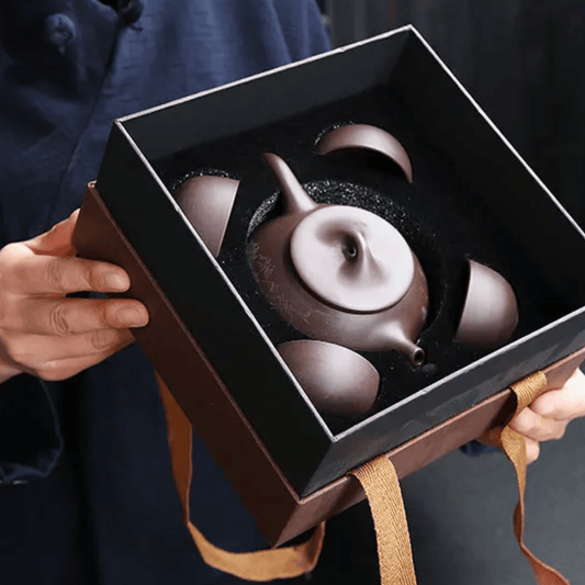 Person holding a black box with a purple teapot inside