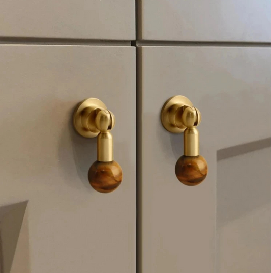 Pair of brass cabinet knobs with brown gemstone sphere handles mounted on white cabinet doors.
