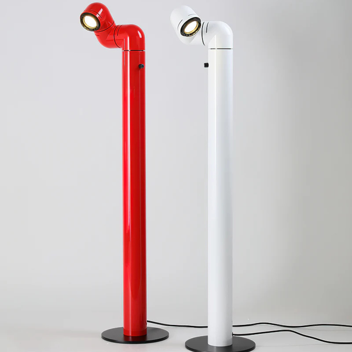 A red and white floor lamp with an angled light fixture, standing on the floor in a minimalist setting.