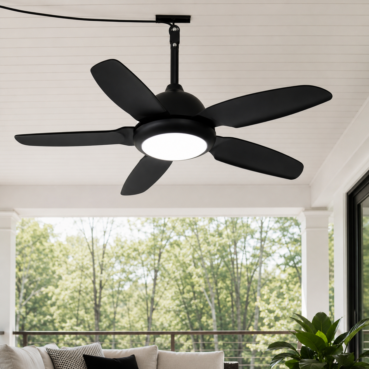 Black ceiling fan with light fixture on a porch with trees in the background