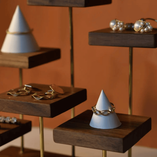 Wooden tiered display with jewelry on white cones against an orange wall