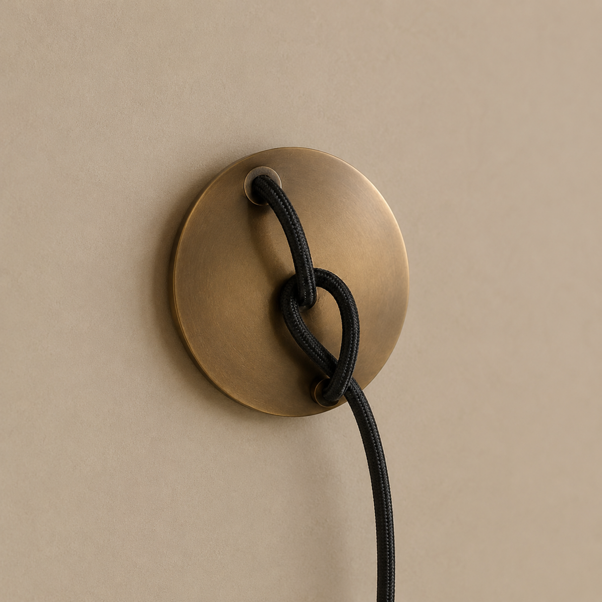 Brass wall fixture with a black cord on a beige background