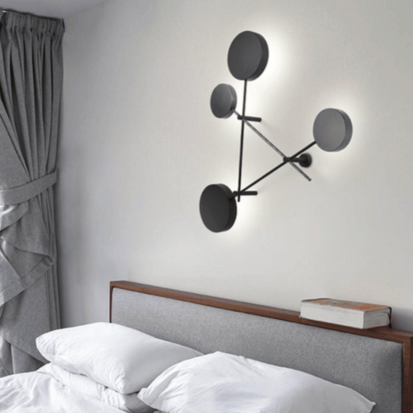 Modern wall lamp with circular design on a white wall above a bed.