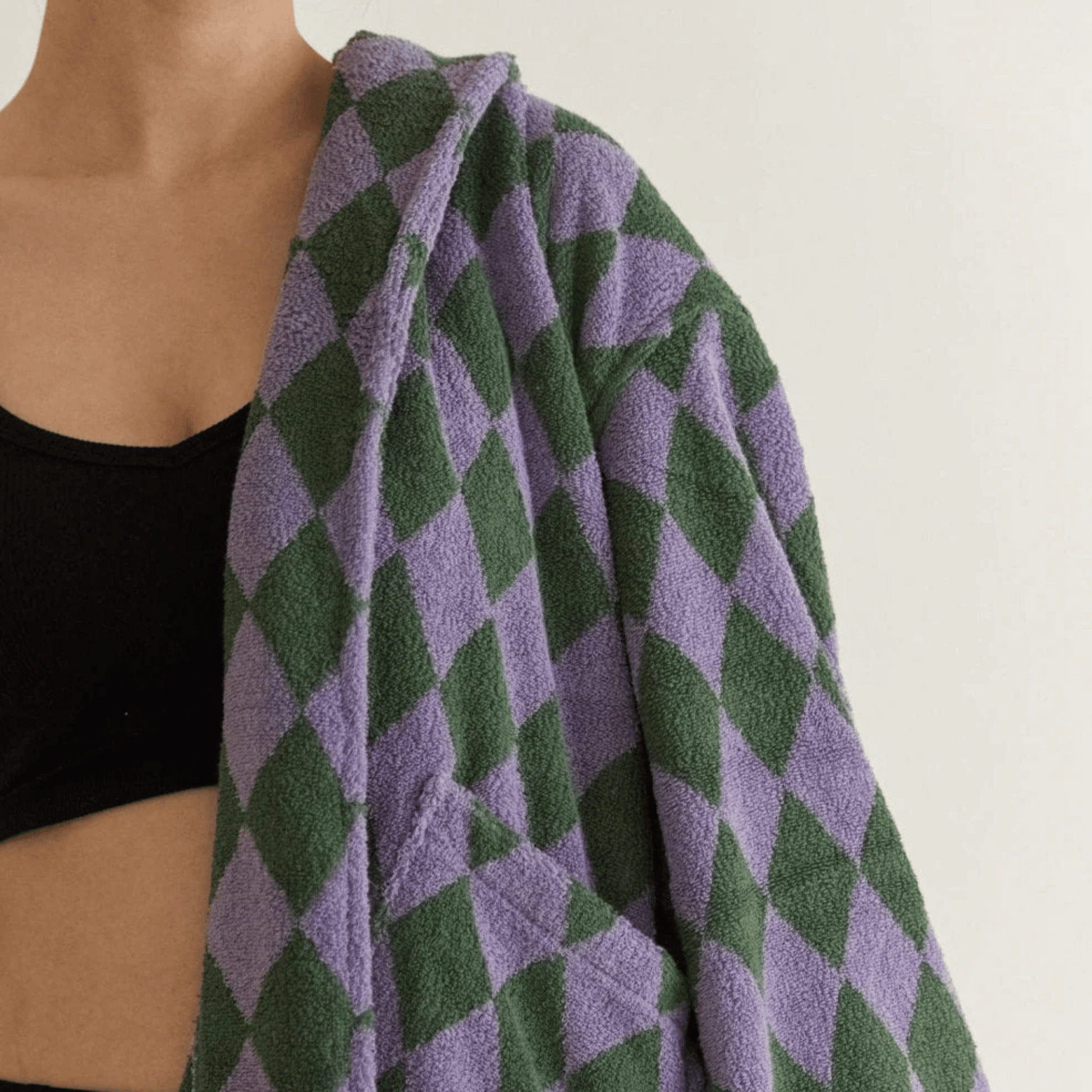 Person wearing a green and purple diamond patterned towel over their shoulder against a white background