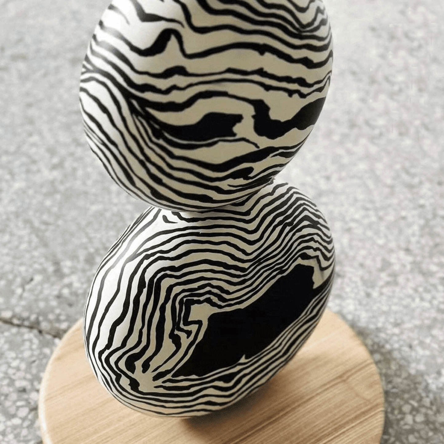 Decorative object with black and white zebra pattern on a wooden stand against a textured gray background
