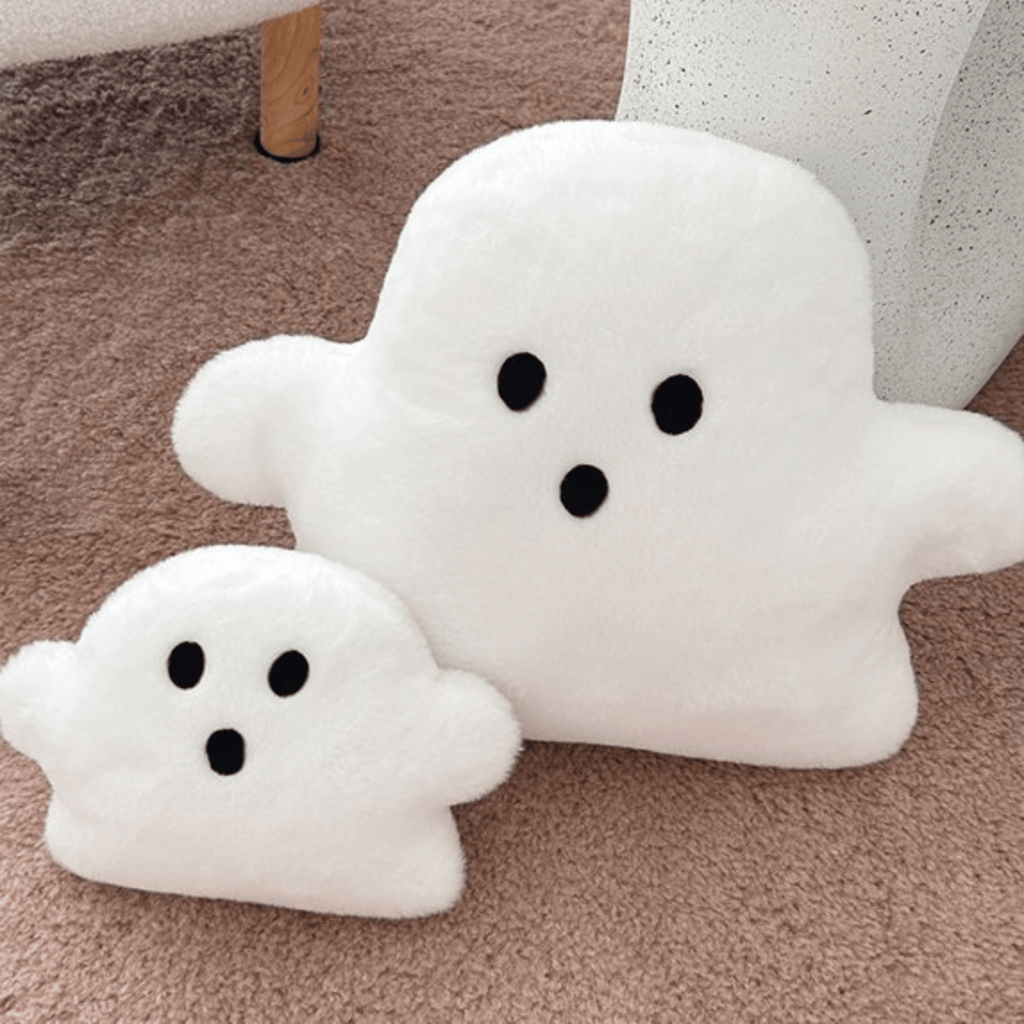 Two white ghost-shaped cushions with black eyes on a beige carpet.