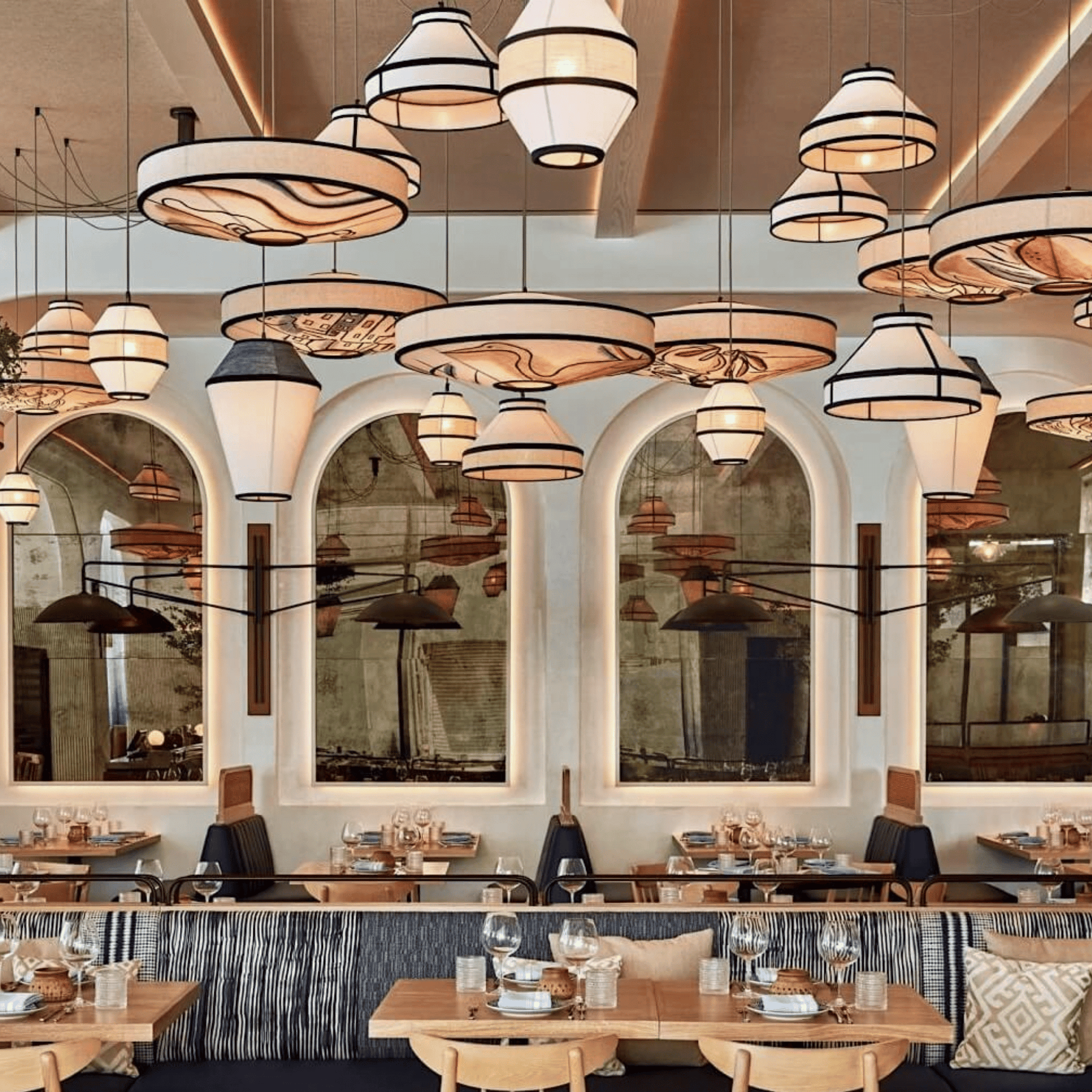 Modern restaurant interior with hanging lights and large mirrors.