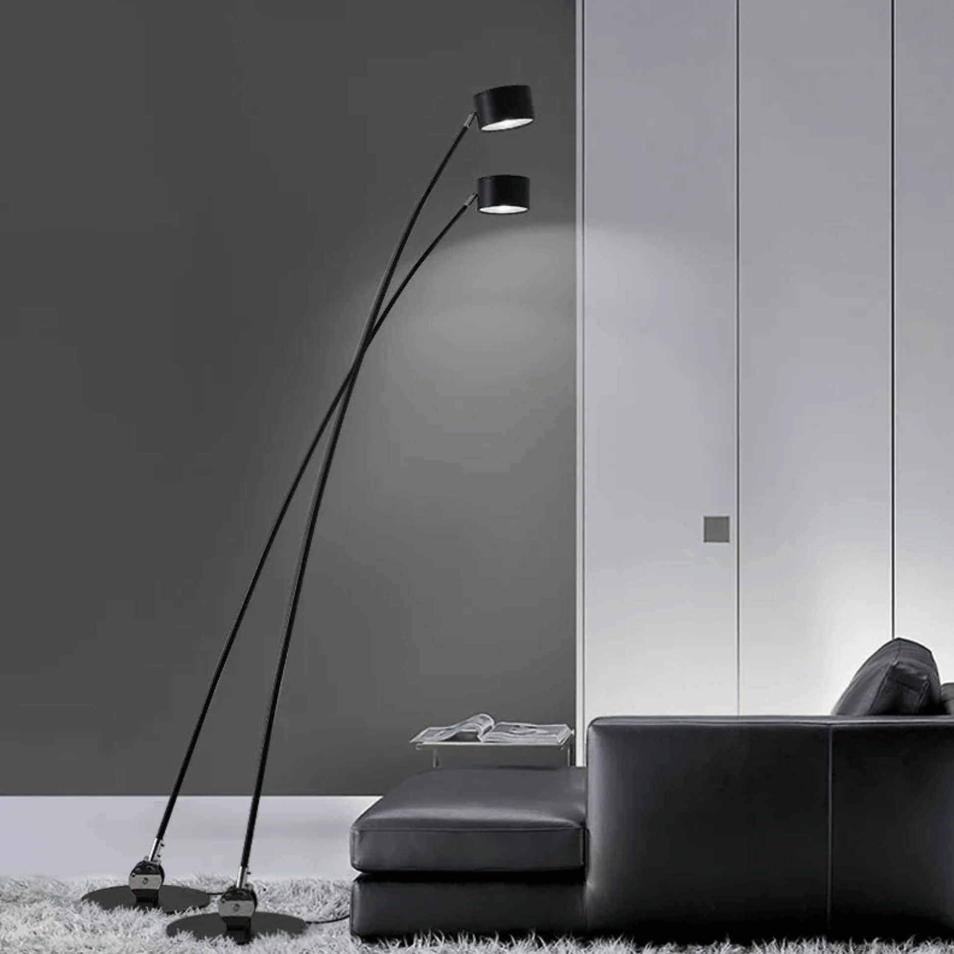 Modern floor lamp with two lights in a minimalistic room with a black sofa.