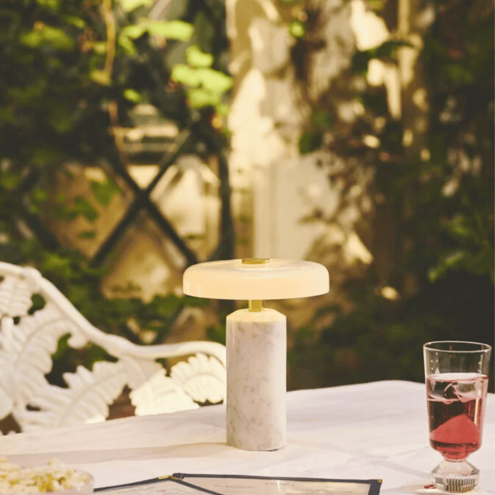 Marble table lamp on a table with a glass of pink drink in a garden setting