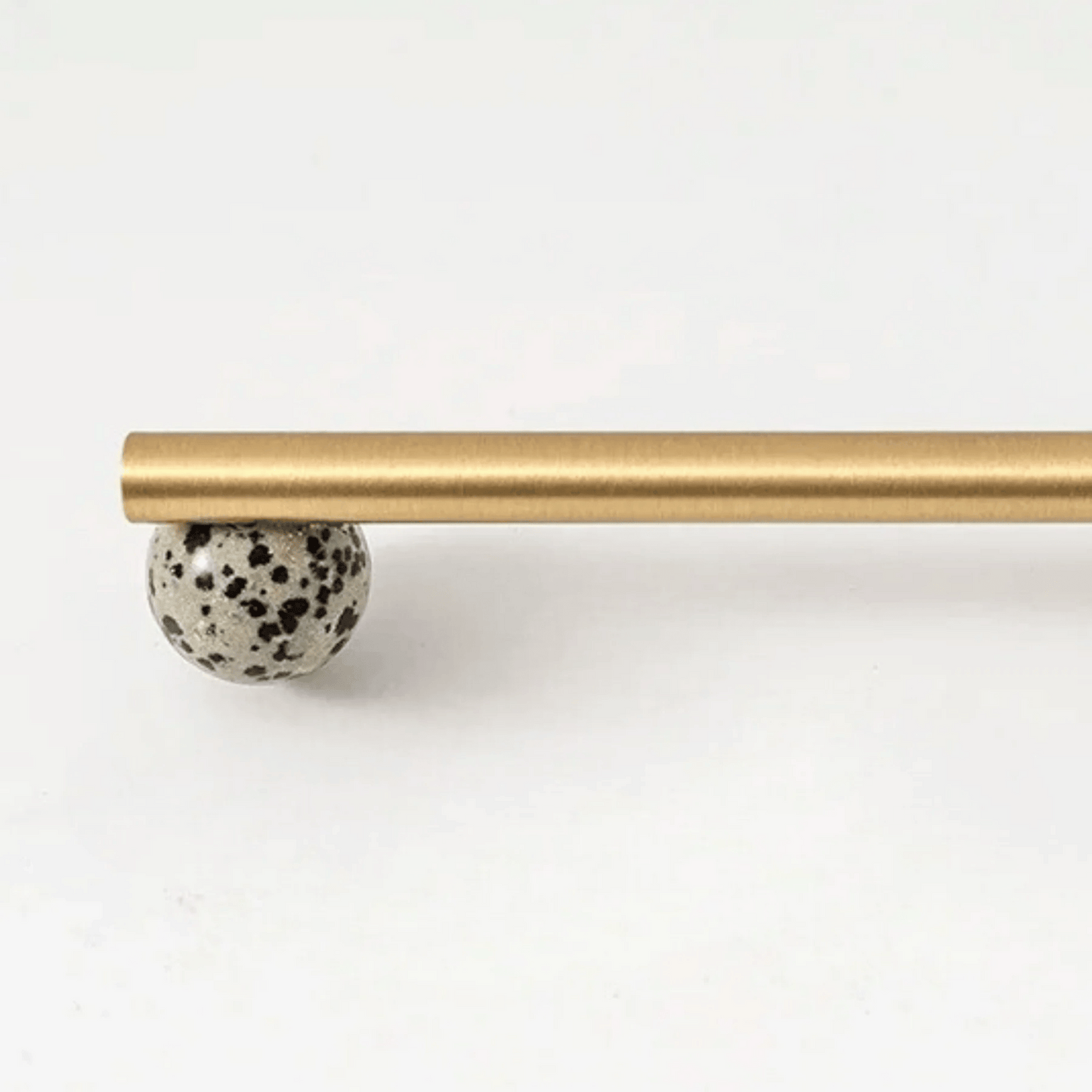 Gold curtain rod with a speckled ball finial on a white background
