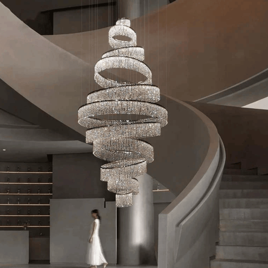 Large spiral chandelier hanging in a modern staircase setting with a woman in a white dress.