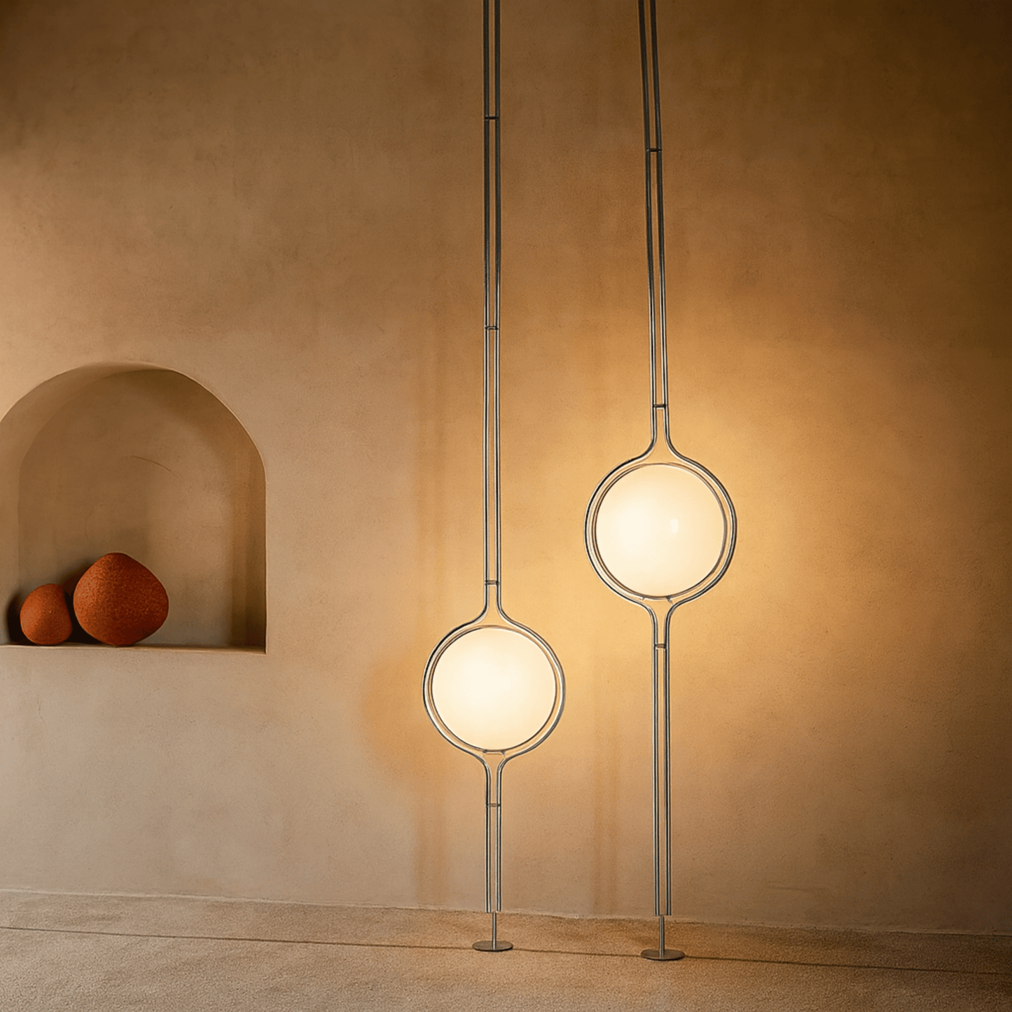 Two modern pendant lights hanging against a beige wall with a shelf displaying three spherical objects.