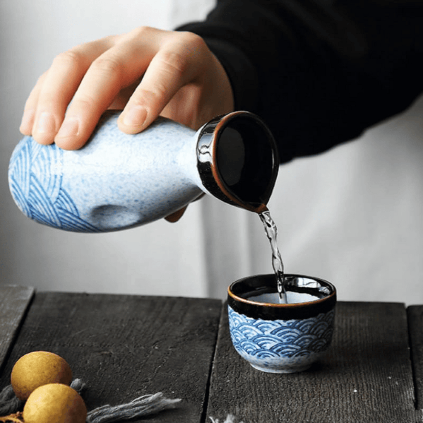 Ceramic teapot being poured into a matching teacup on a wooden surface.