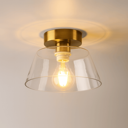 Ceiling light fixture with gold finish and clear glass shade on a neutral background