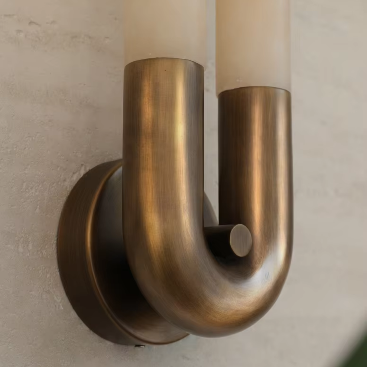 Brass wall sconce with two cylindrical lights on a neutral wall.