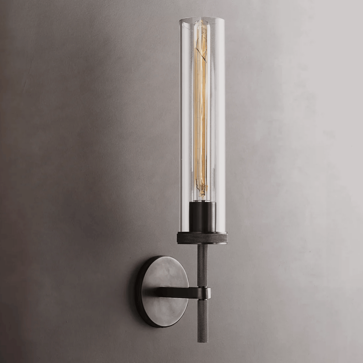 Modern wall-mounted light fixture with clear cylindrical glass shade on a gray background
